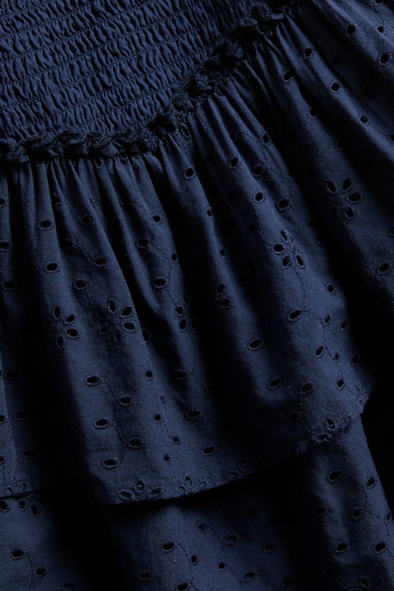 Lähikuva sinisestä lyhyestä hameesta, jossa on smock-vyötärö ja kerrostettu broderie anglaise -kangas.