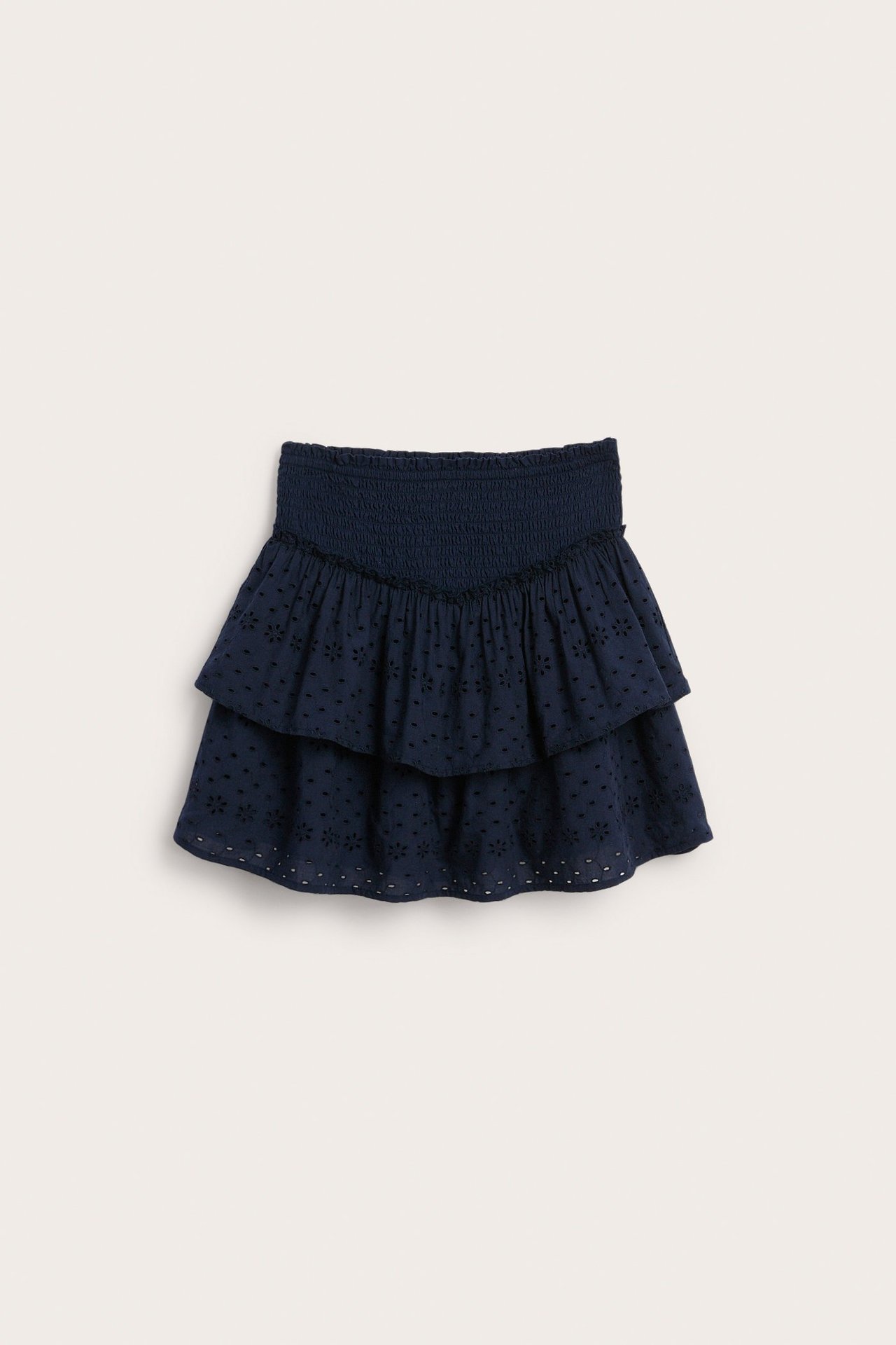 Edestä näkymä lasten tummansinisestä hameesta, jossa broderie anglaise -kuvio, kaksi röyhelöä ja smock-vyötärö.