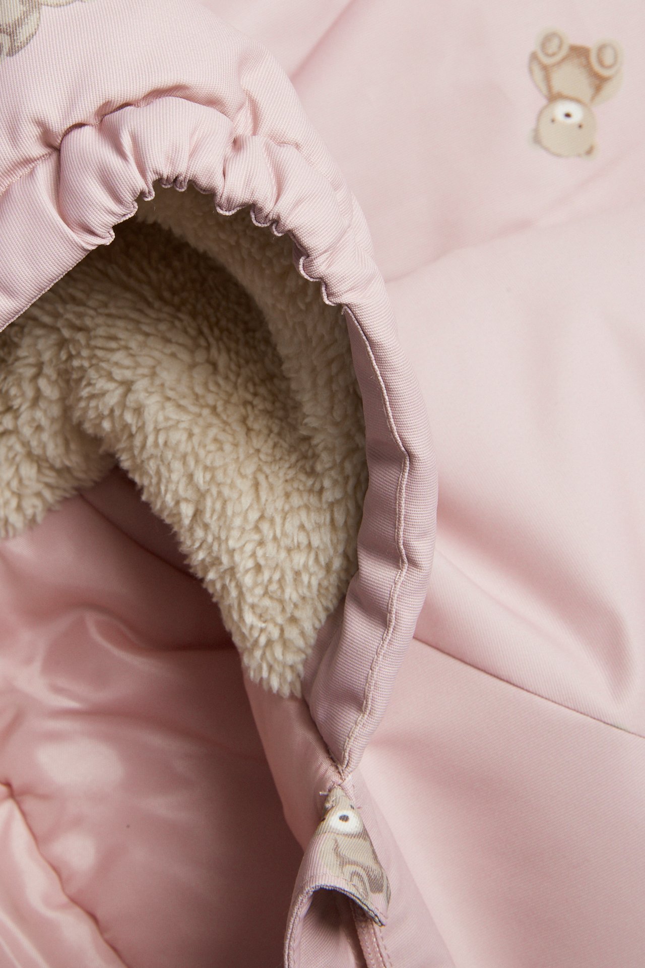 Nærbilde av en rosa babysovepose med beige plysjfôr og broderte bjørner.