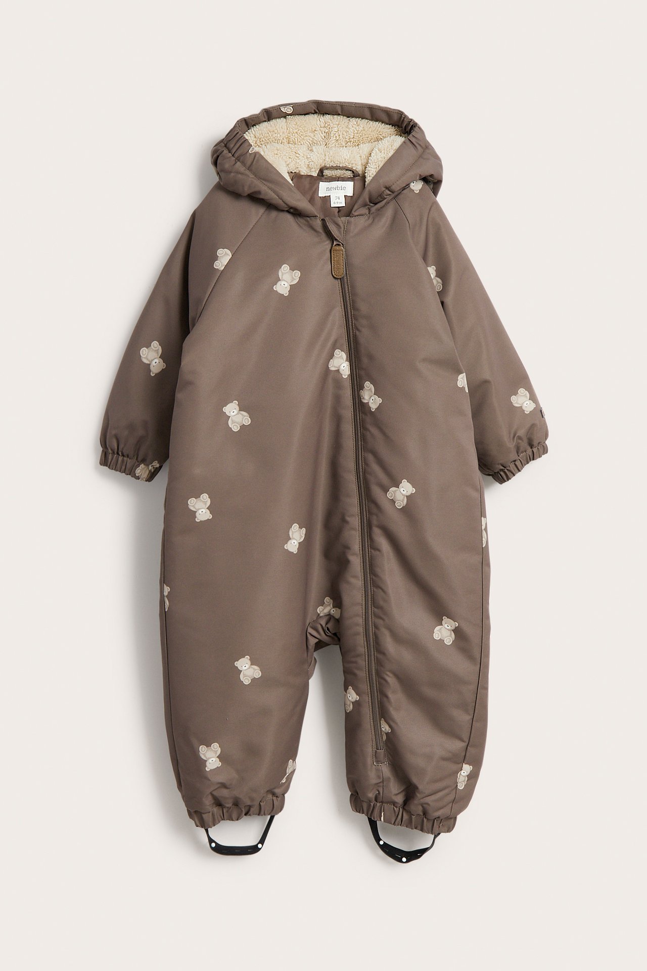 Framifrån, brun babyoverall med huva, teddybjörnsmönster och dragkedja fram.