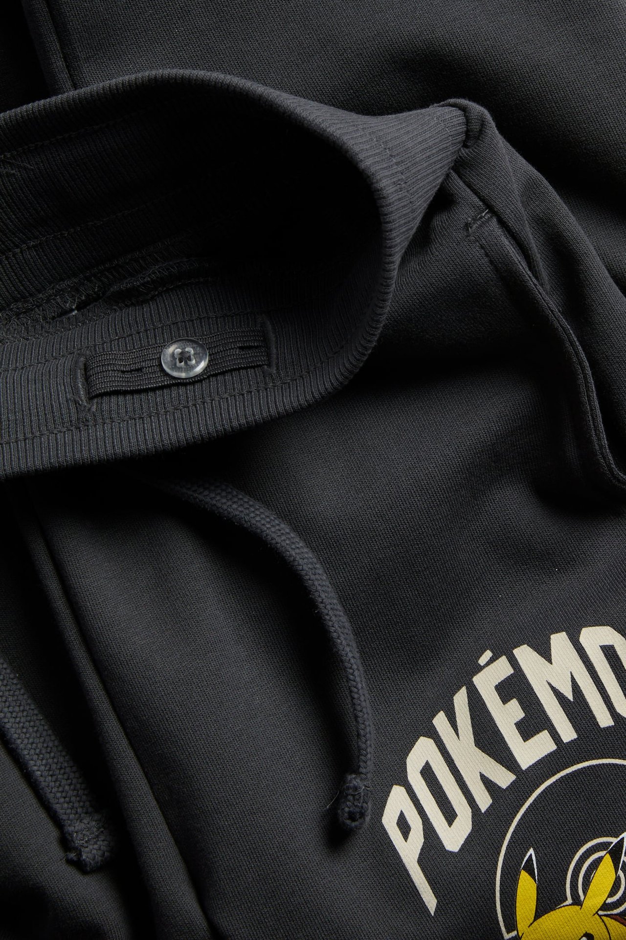 Zbliżenie czarnych spodni dresowych Pokémon z elastycznym pasem, guzikiem i sznurkiem.