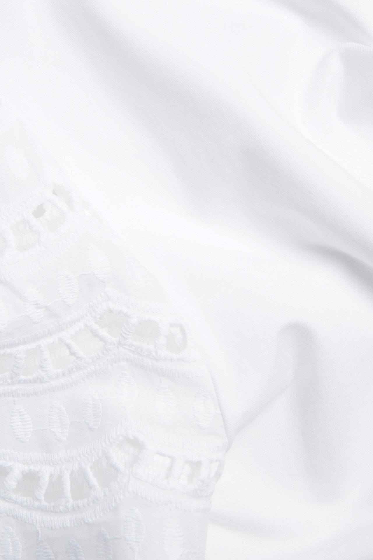 Lähikuva valkoisesta puuvillatopista, jossa on broderie anglaise -yksityiskohtia lyhyissä hihoissa.