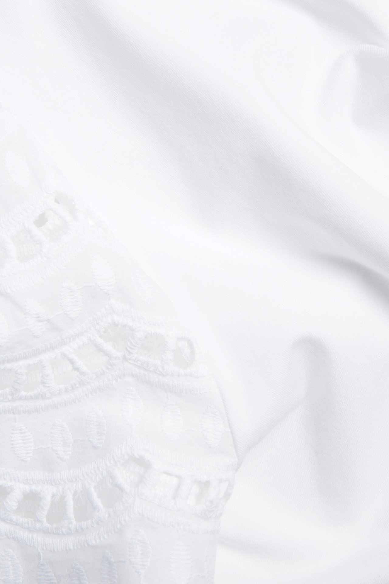Lähikuva valkoisesta puuvillatopista, jossa on broderie anglaise -yksityiskohtia lyhyissä hihoissa.