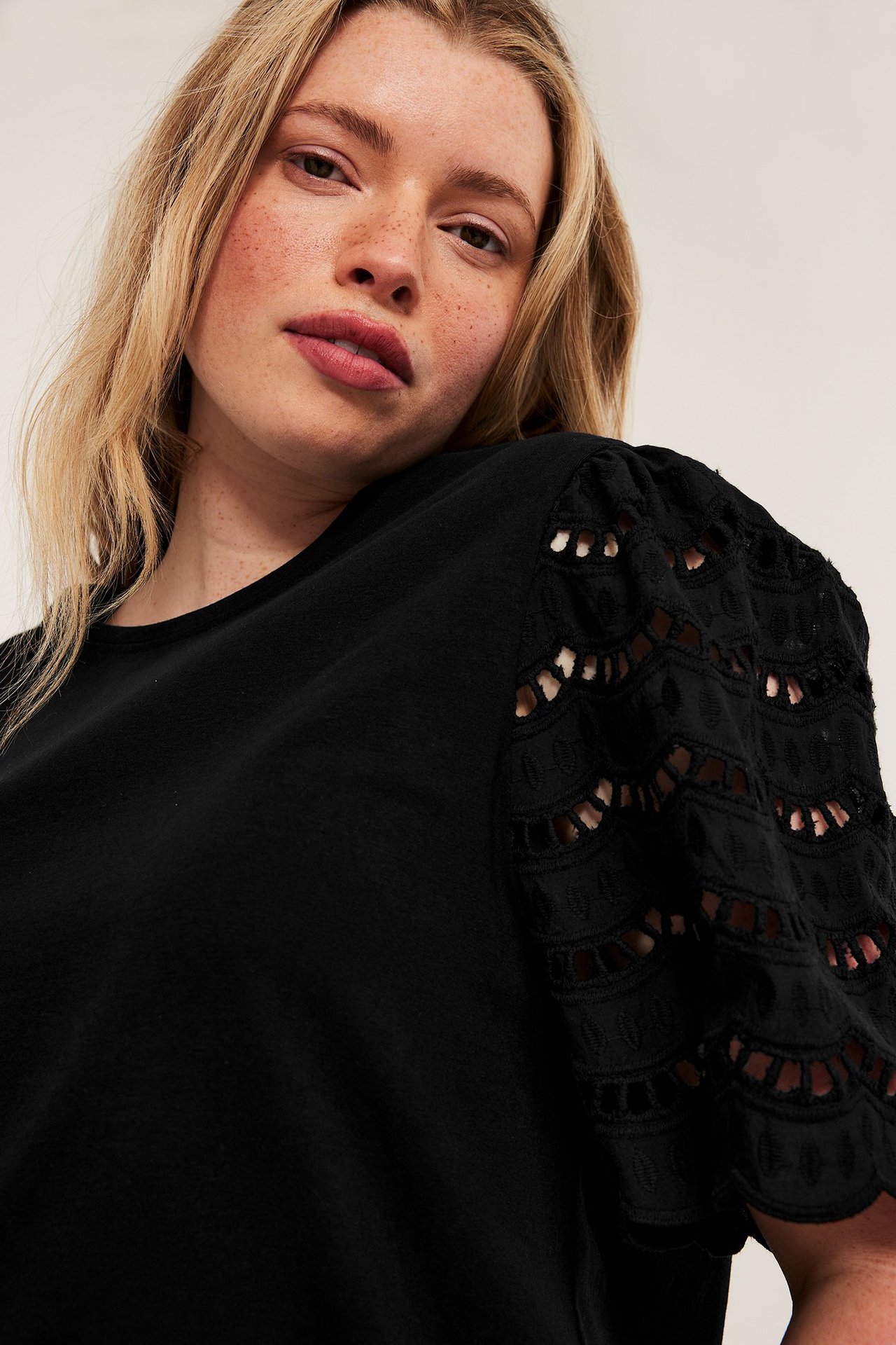 Lähikuva naisesta yllään musta toppi lyhyillä broderie anglaise -hihoilla.
