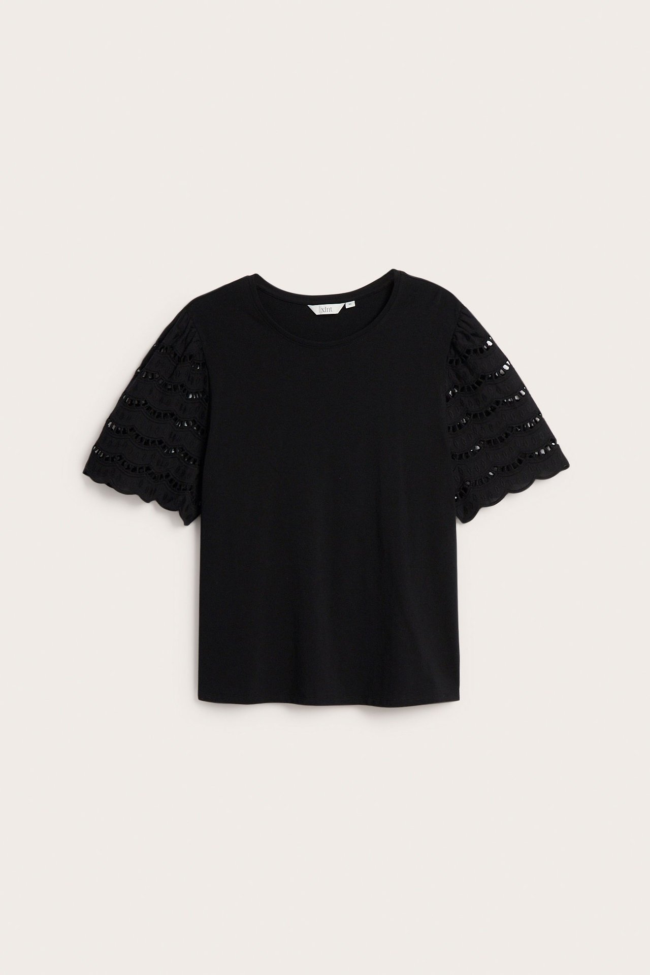 Edestä päin musta lantiopituinen toppi lyhyillä broderie anglaise -hihoilla ja pyöreällä pääntiellä.