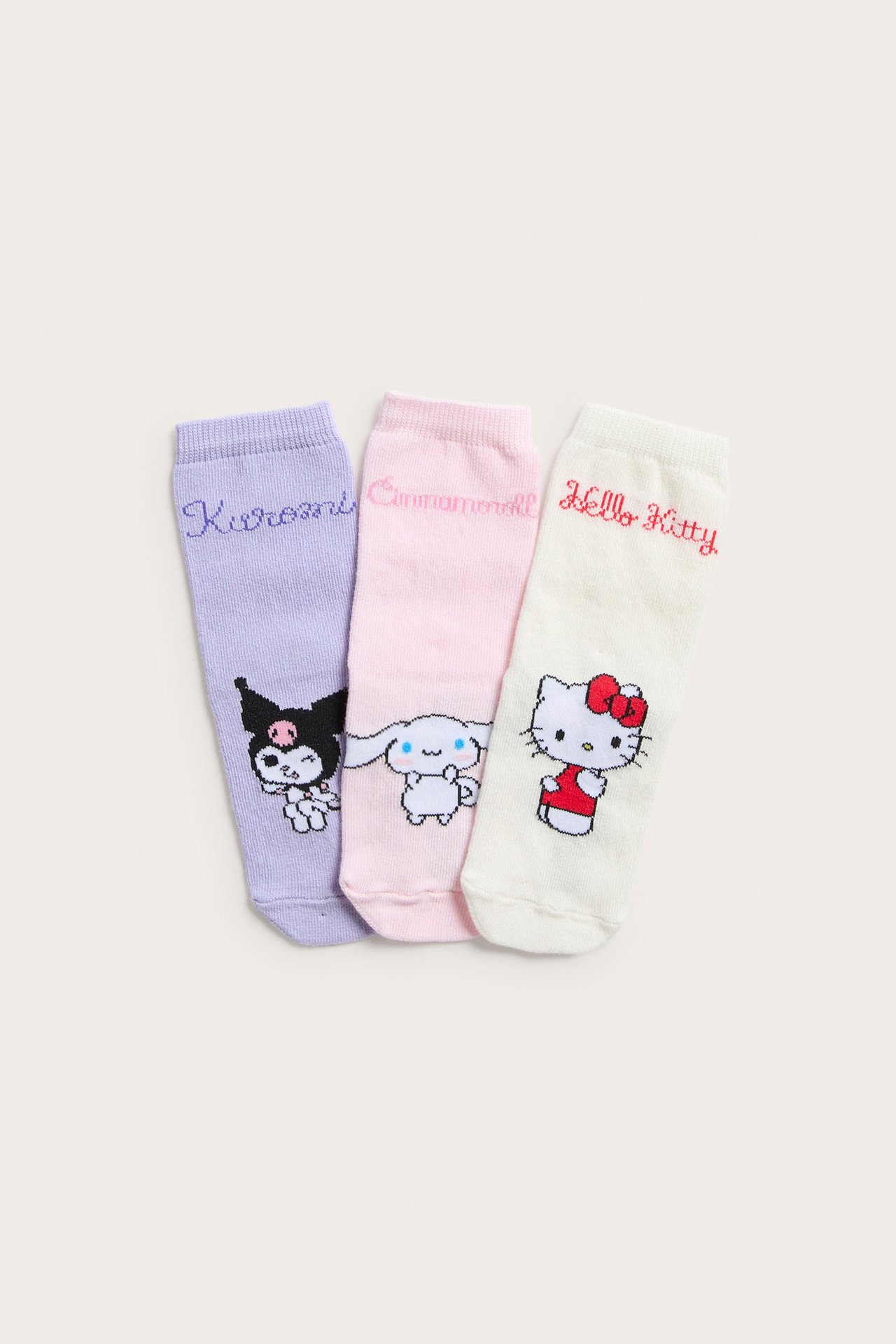 Widok z przodu trzech skarpetek dziecięcych: ecru Hello Kitty, jasnoróżowe Cinnamoroll i jasnofioletowe Kuromi.