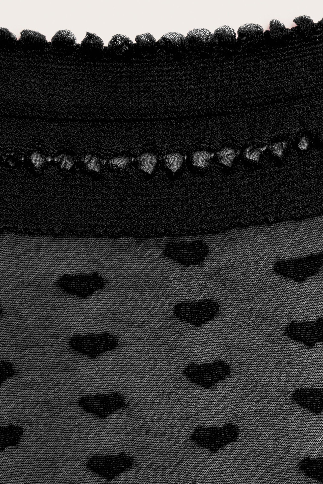 Nærbilde av en svart, gjennomsiktig sokk med volangkant og ugjennomsiktig hjertemønster.