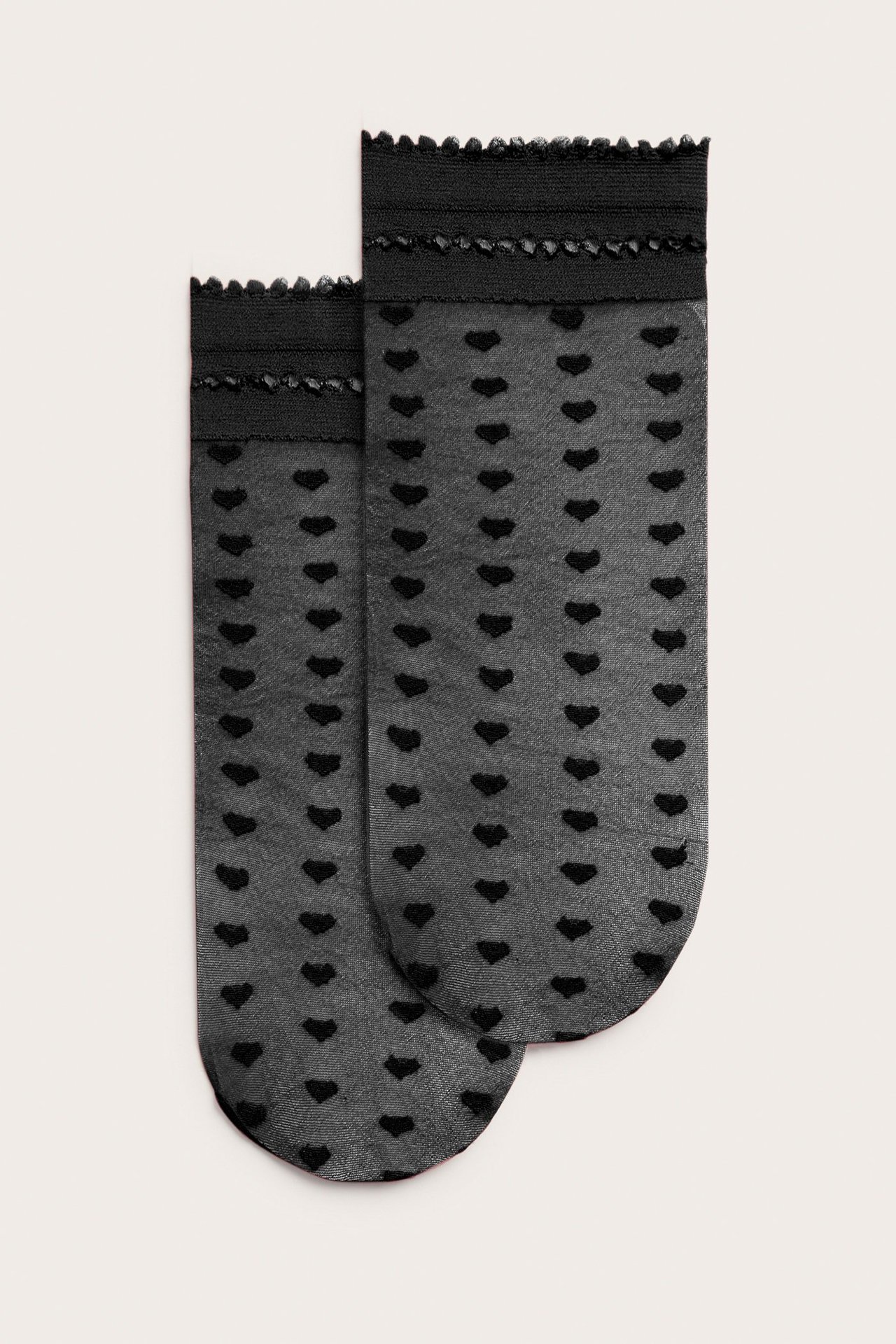 Forfra to svarte tynne polyamidstrømper med små hjertemønstre og rysjekanter.