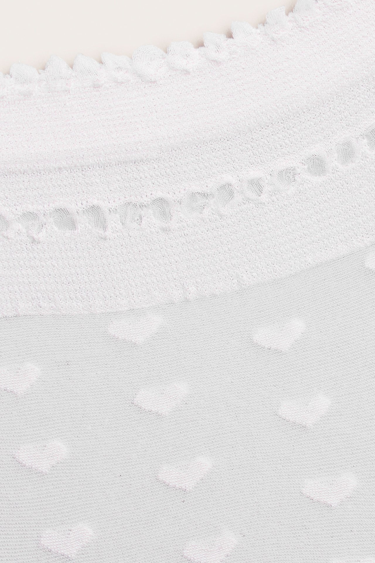 Nærbilde av offwhite tynne sokker med et hevet hjertemønster og en delikat bølget kant.
