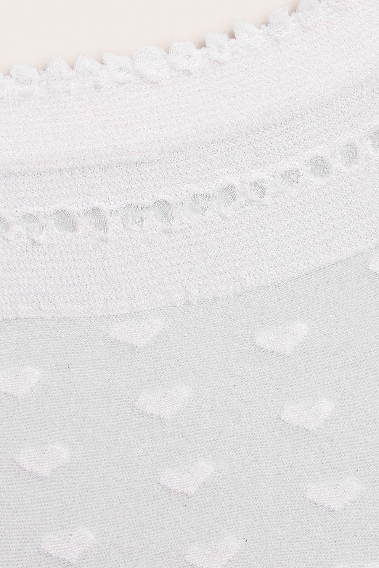 Nærbilde av offwhite tynne sokker med et hevet hjertemønster og en delikat bølget kant.