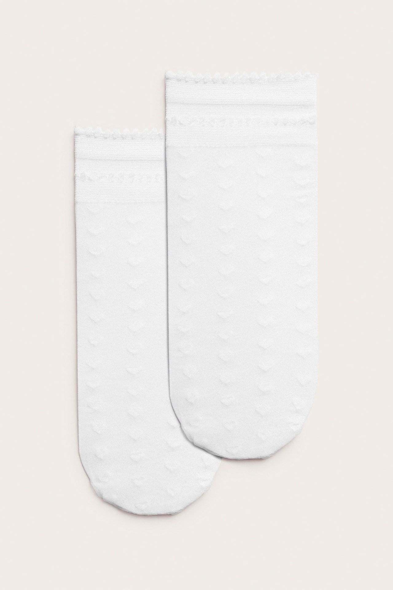 Forfra, to offwhite tynne ankelsokker med diskret hjertemønster og volangkant.