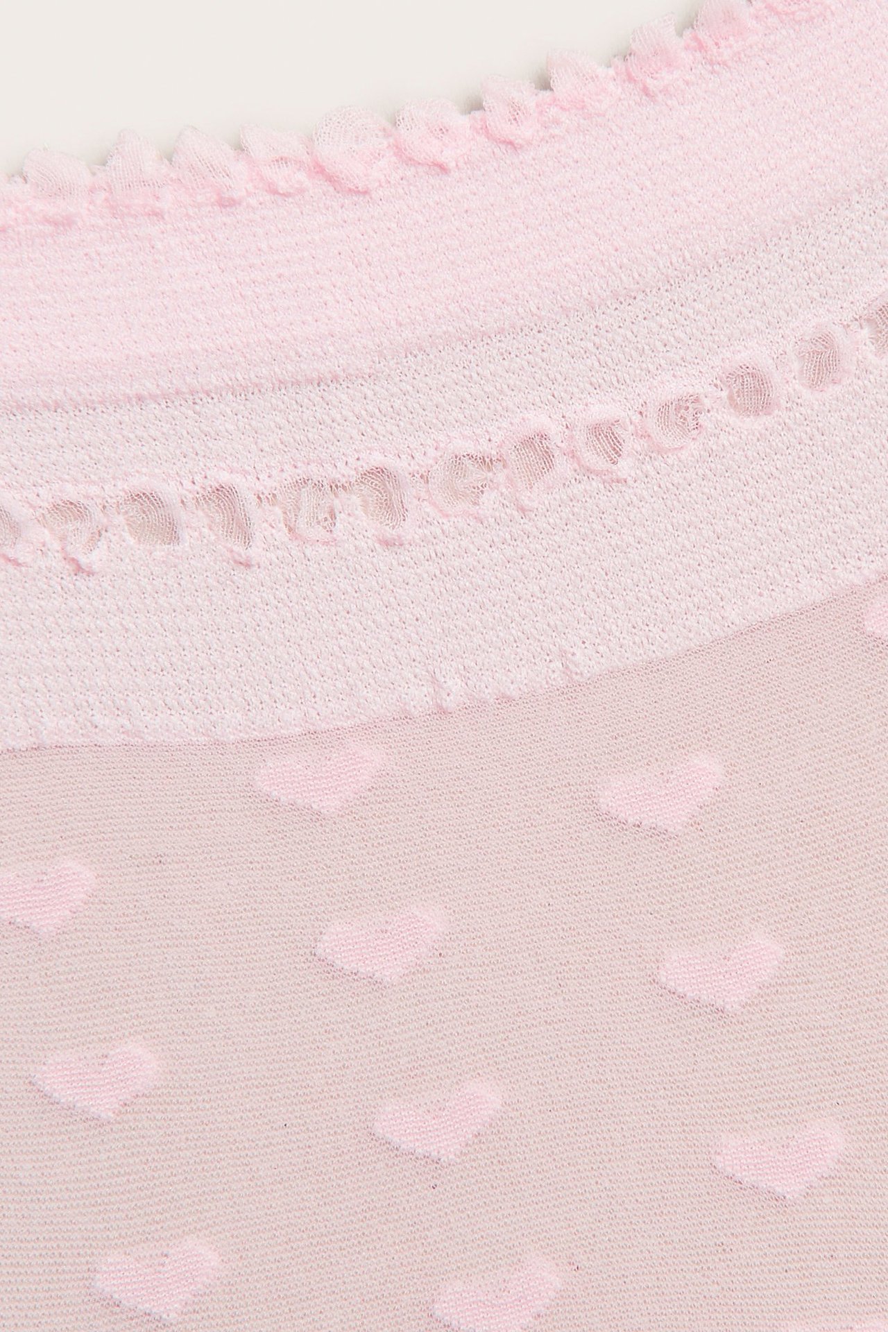 Nærbilde av en lyserosa gjennomsiktig sokk med volangkant, hullmønstret bånd og hjertemønster.