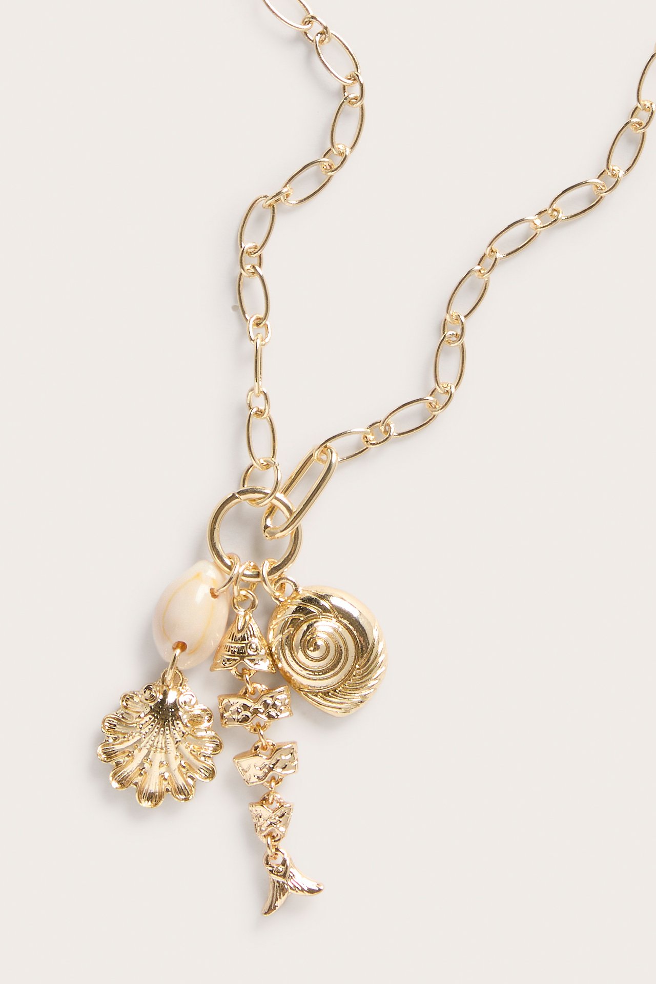 Lähikuva kultaisesta metallikaulakorusta, jossa on ovaali ketju ja useita simpukka- ja kalanhäntäriipuksia.