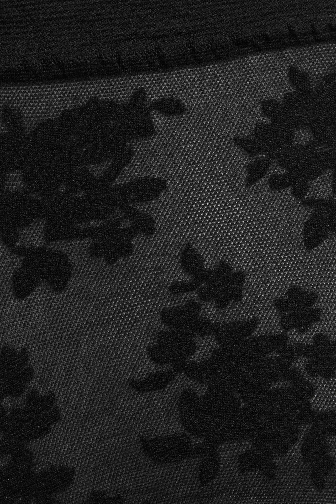 Nærbilde av en svart gjennomsiktig sokk med opphøyet blomstermønster og elastisk kant øverst.