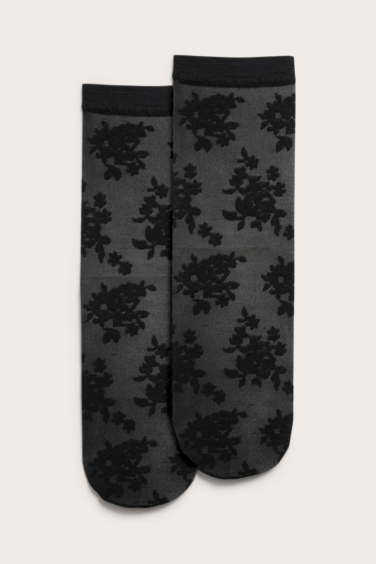Forfra to tynne svarte sokker med svart blomstermønster.
