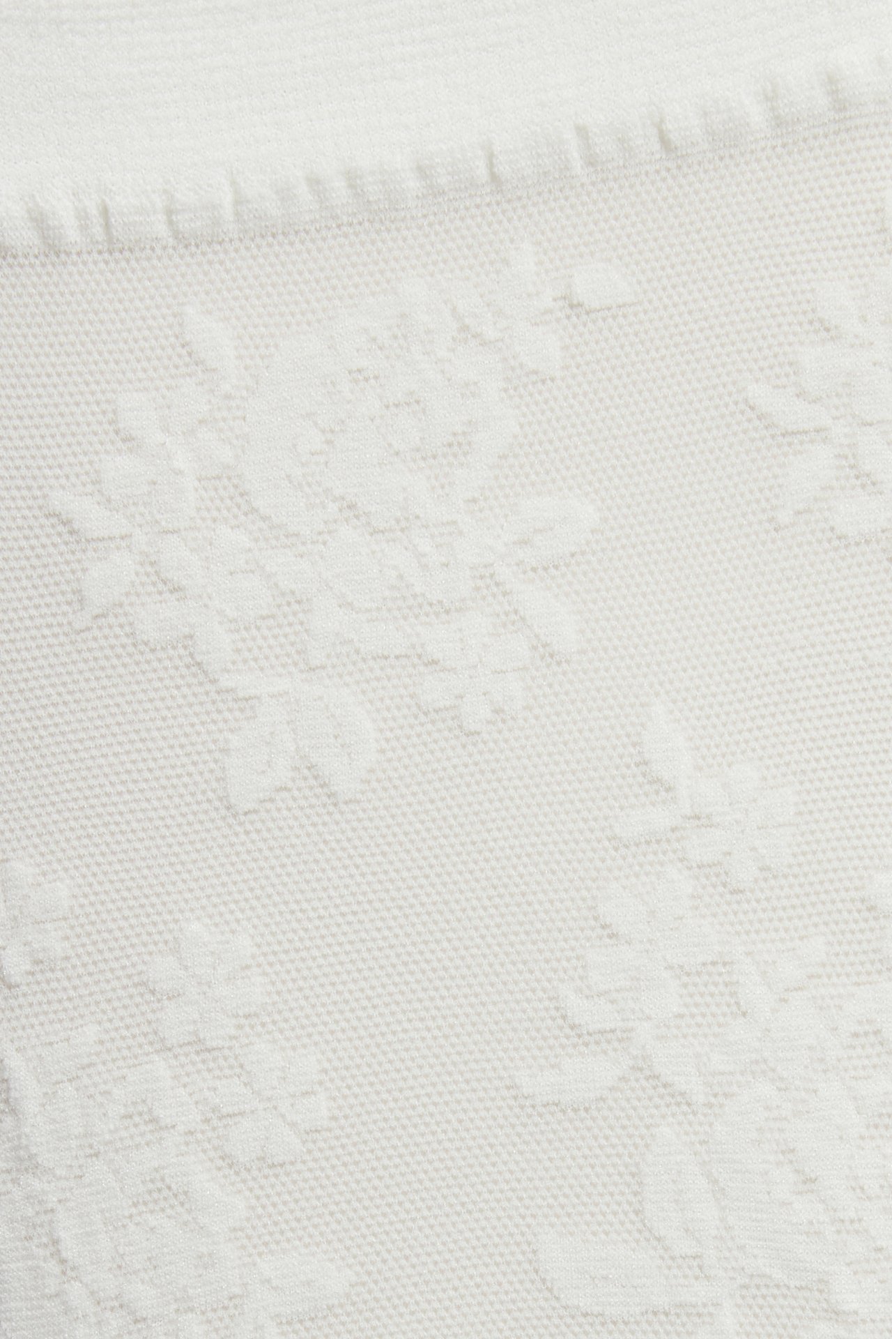 Nærbilde av off-white tynt sokkestoff med et preget blomstermønster.