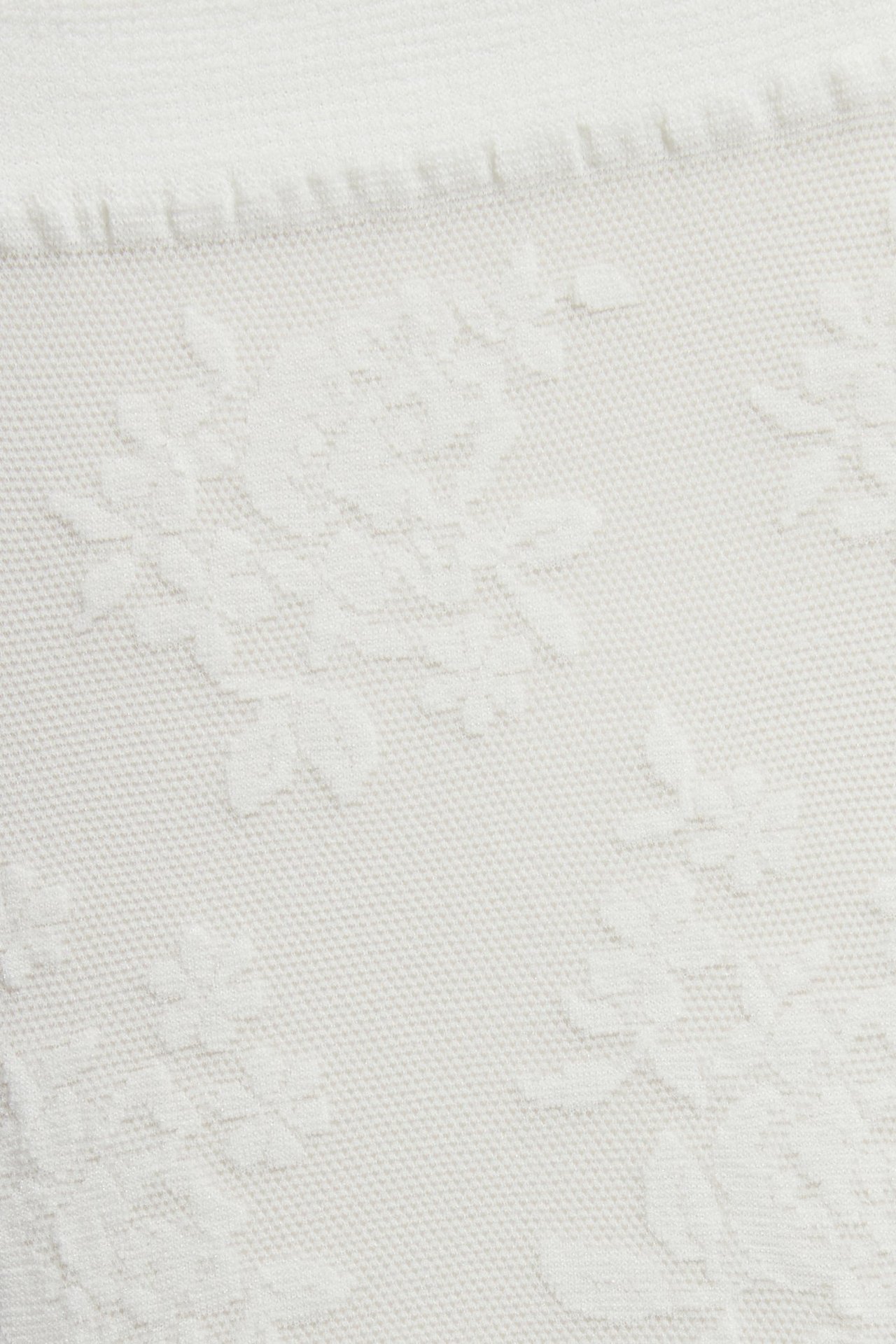 Nærbilde av off-white tynt sokkestoff med et preget blomstermønster.