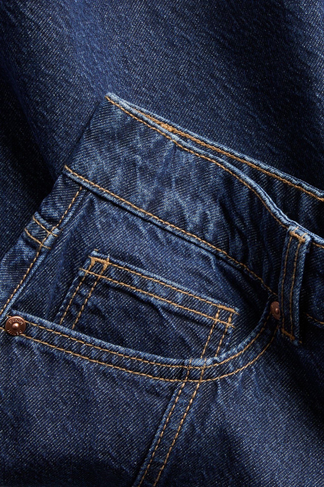 Nærbilde av mørkeblå A-linjeformet jeansskjørt, med synlige frontlommer, brune sømmer og metallnagler.