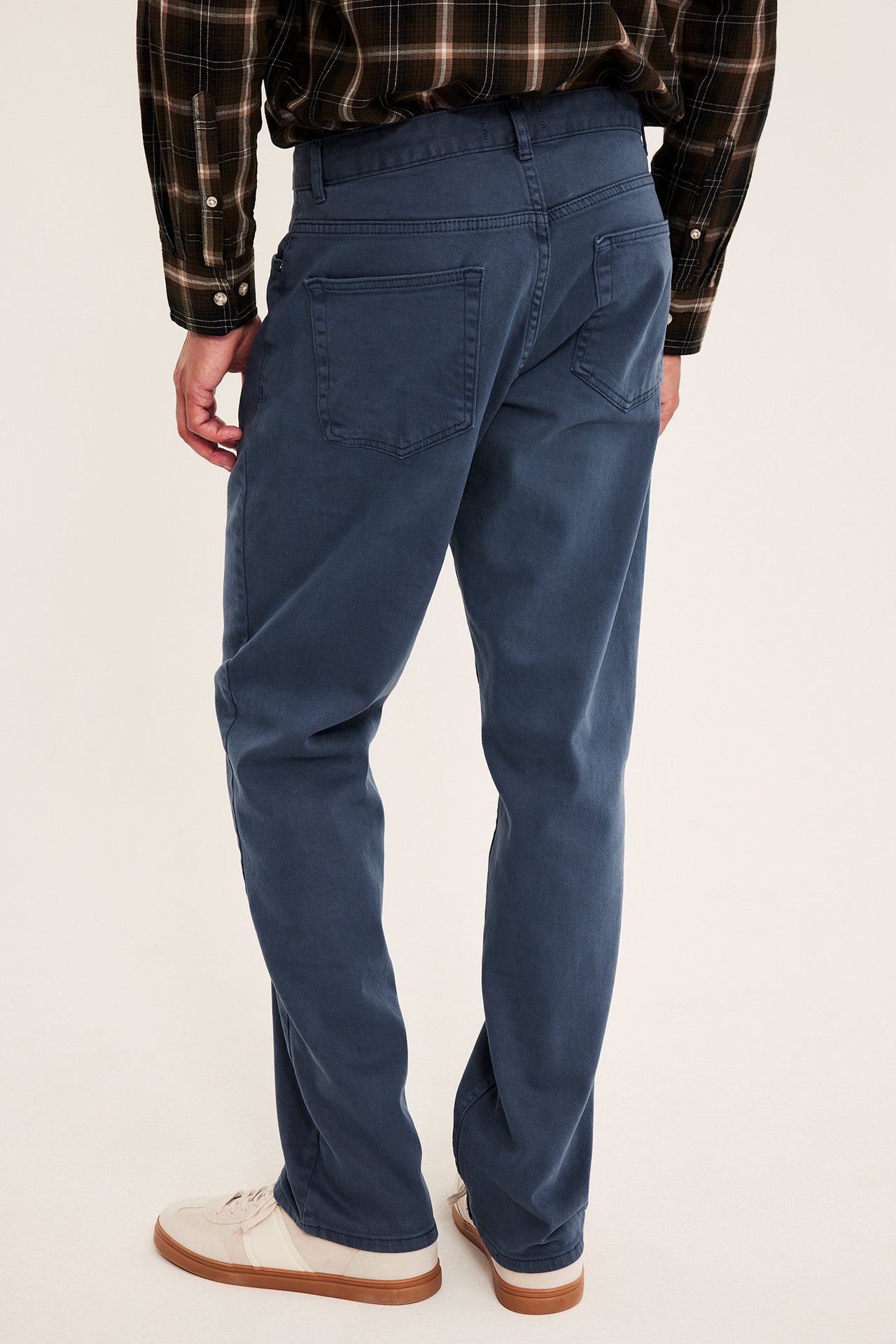 Bakfra: Mann i blå jeans, mørk rutete langermet skjorte og beigefargede joggesko.