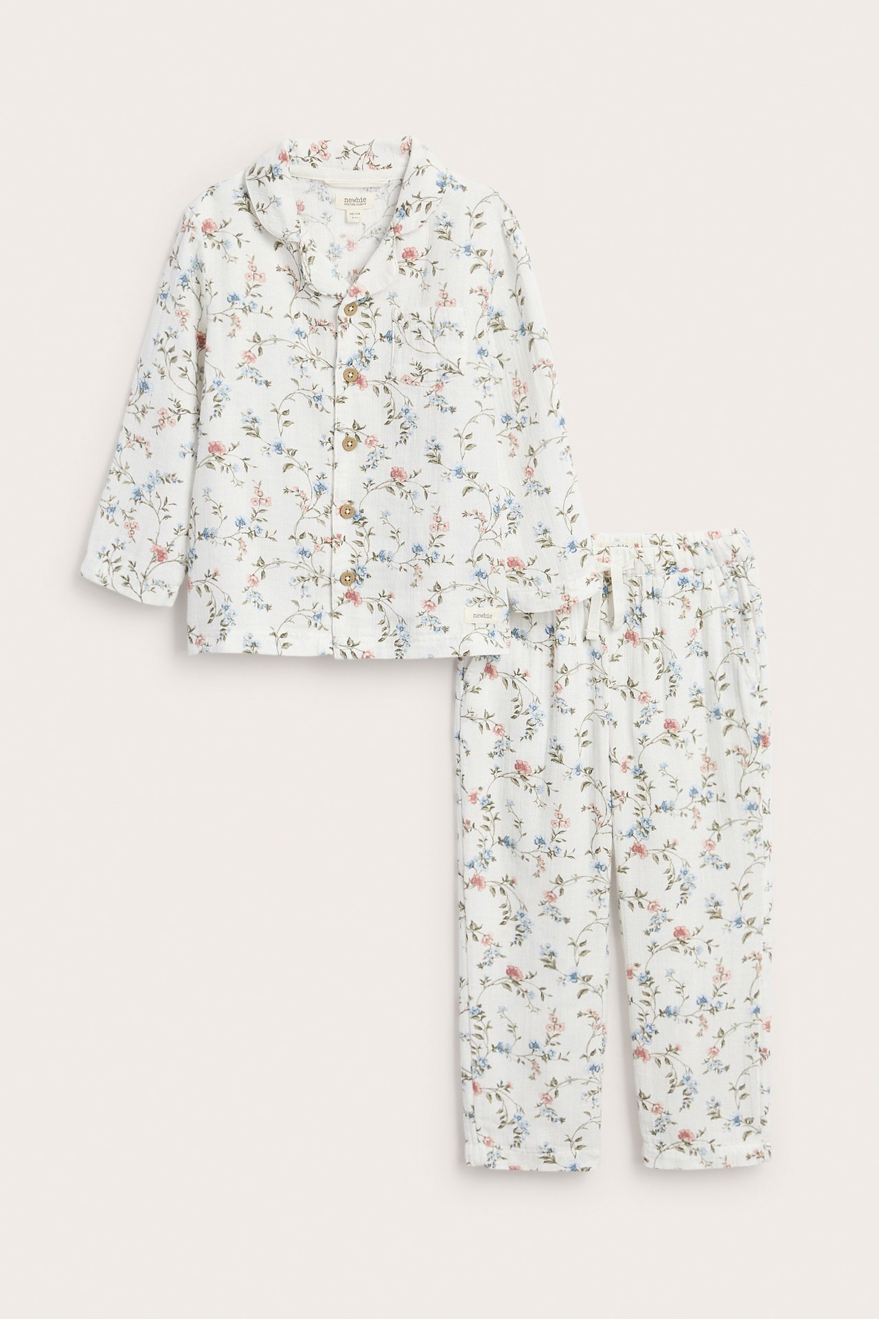 Frontvy av en offwhite tvådelad pyjamas i bomull för barn med blått och rosa blommigt mönster.