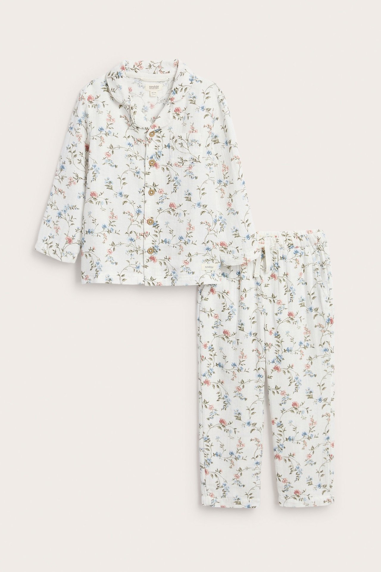 Frontvy av en offwhite tvådelad pyjamas i bomull för barn med blått och rosa blommigt mönster.