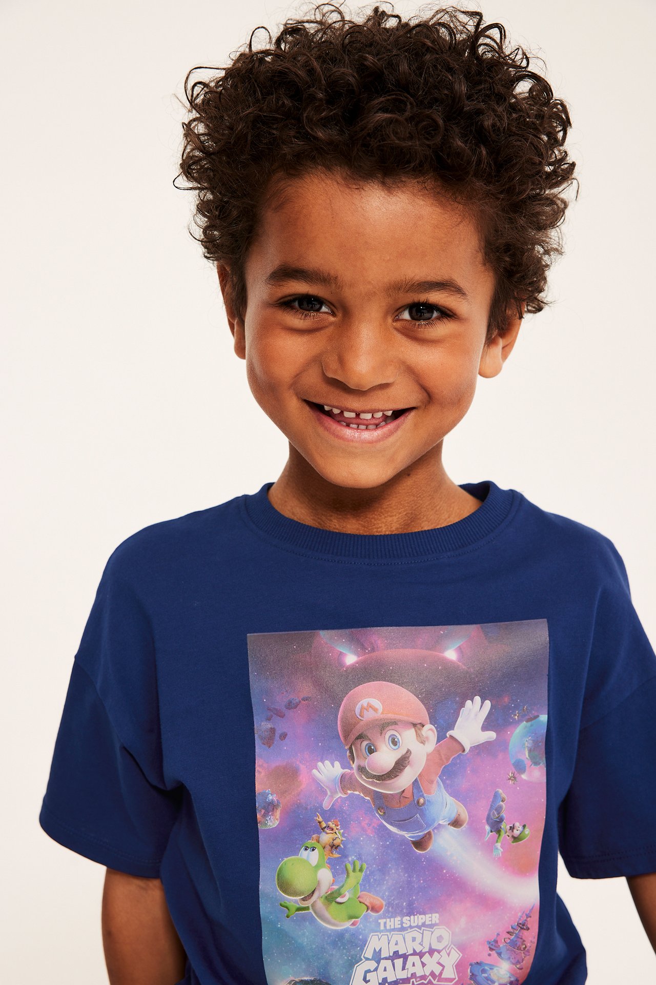 Widok z przodu uśmiechniętego dziecka w granatowej koszulce bawełnianej Super Mario Galaxy z nadrukiem.