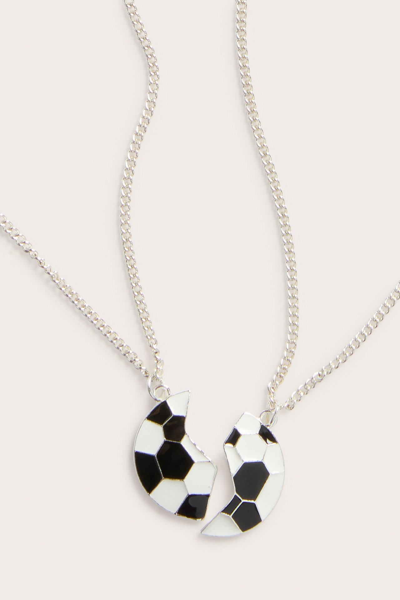 Nærbilde forfra av to sølvfargede metall BFF-halskjeder med matchende svart-hvite fotballanheng.