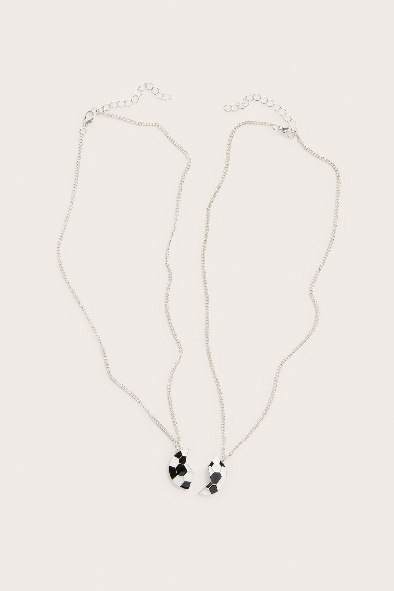 Lähikuva kahdesta hopeanvärisestä metallisesta ystävyyskaulakorusta, joissa puolikas mustavalkoinen jalkapalloriipus.