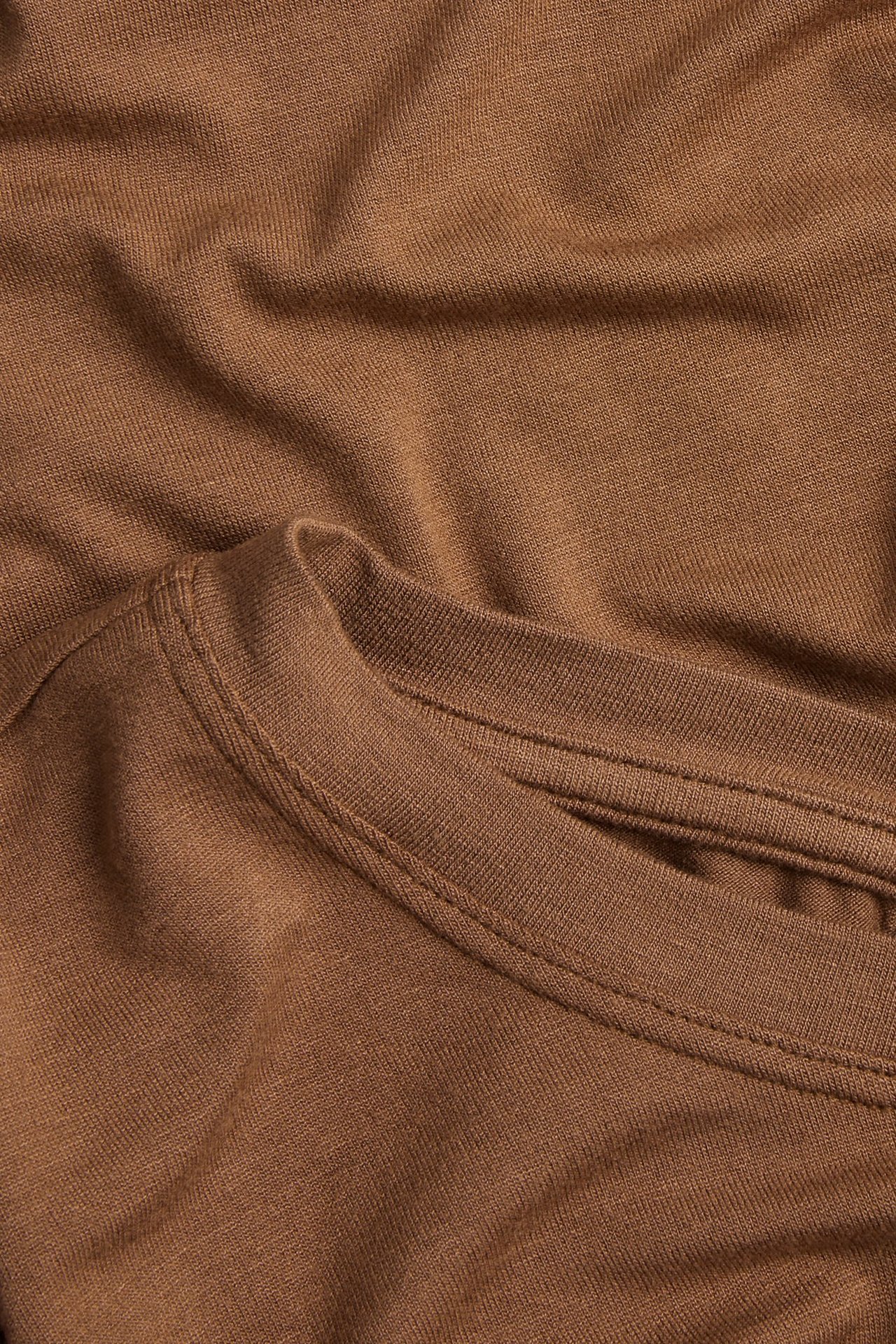 Närbild av en brun, enfärgad långärmad topp i ett draperat viskosblandat tyg.