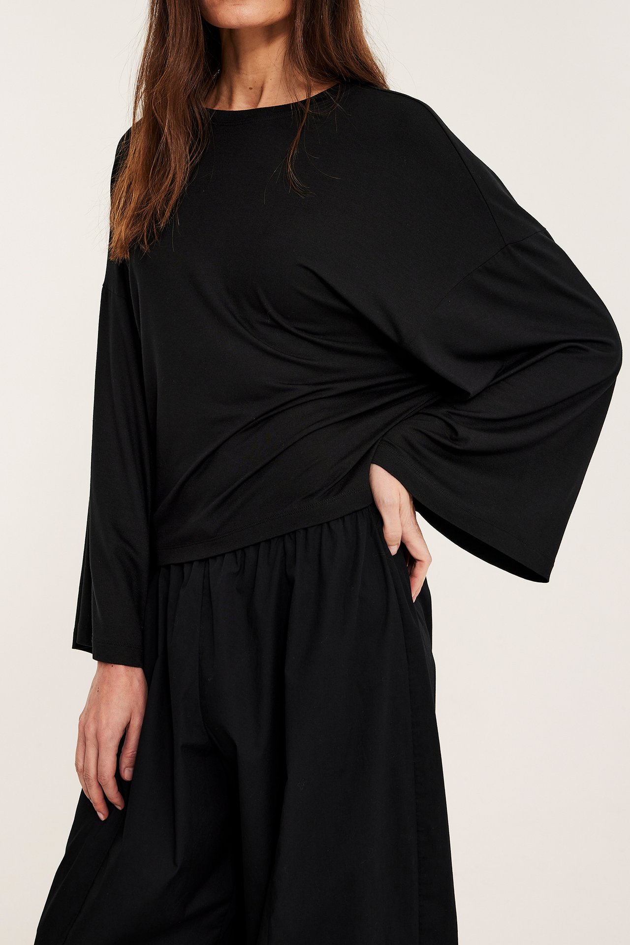 Framifrån: Kvinna i svart draperad långärmad topp med vida ärmar och svarta vida byxor.