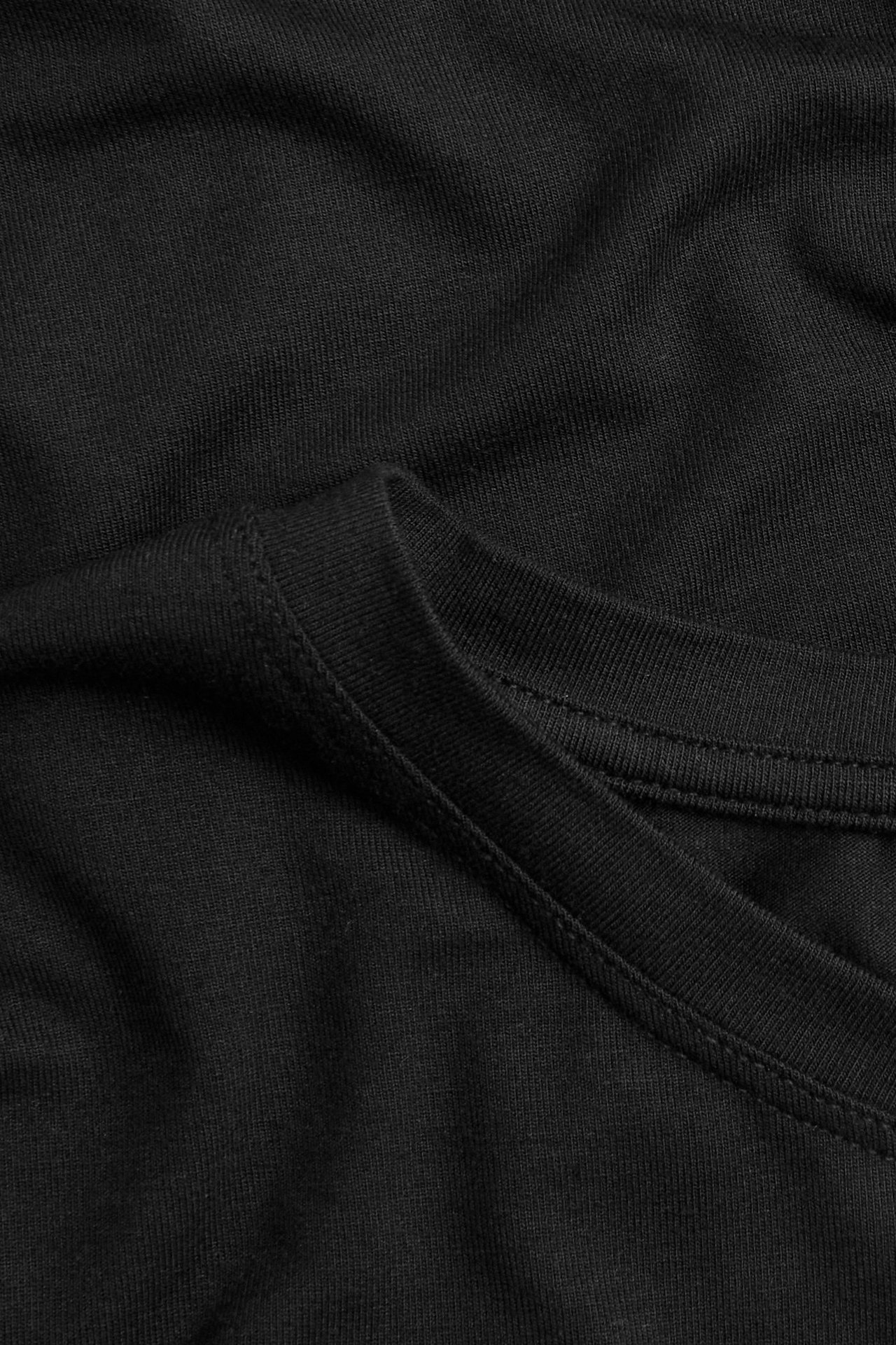 Närbild av en svart långärmad topp i mjukt, draperat viskosblandat tyg med synlig söm.