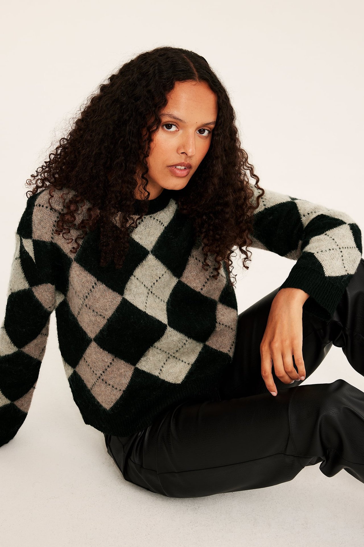 Naisen etukuva, yllään vihreä, beige ja harmaa argyle-neule sekä mustat tekonahkahousut.