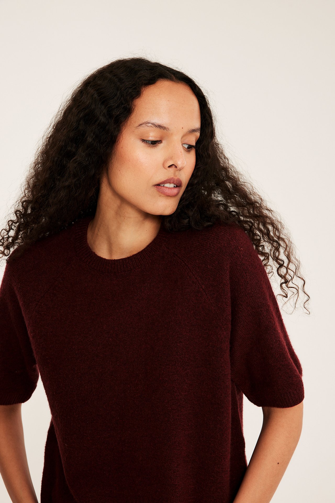 Närbild framifrån på en kvinna i en melerad, vinröd oversized stickad t-shirt med korta ärmar.