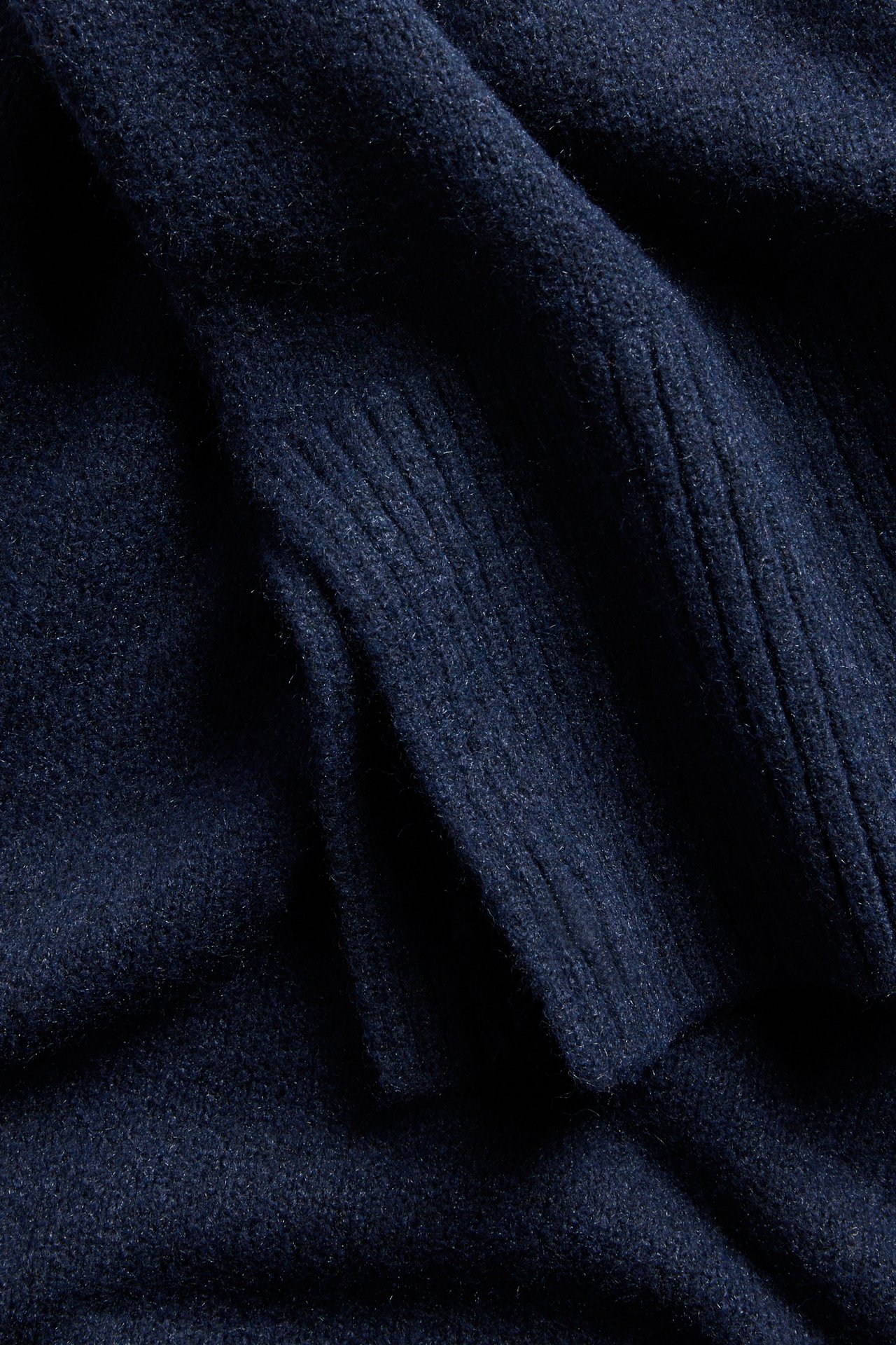 Närbild av en mörkblå melerad stickad pullover med synliga ribbade detaljer.