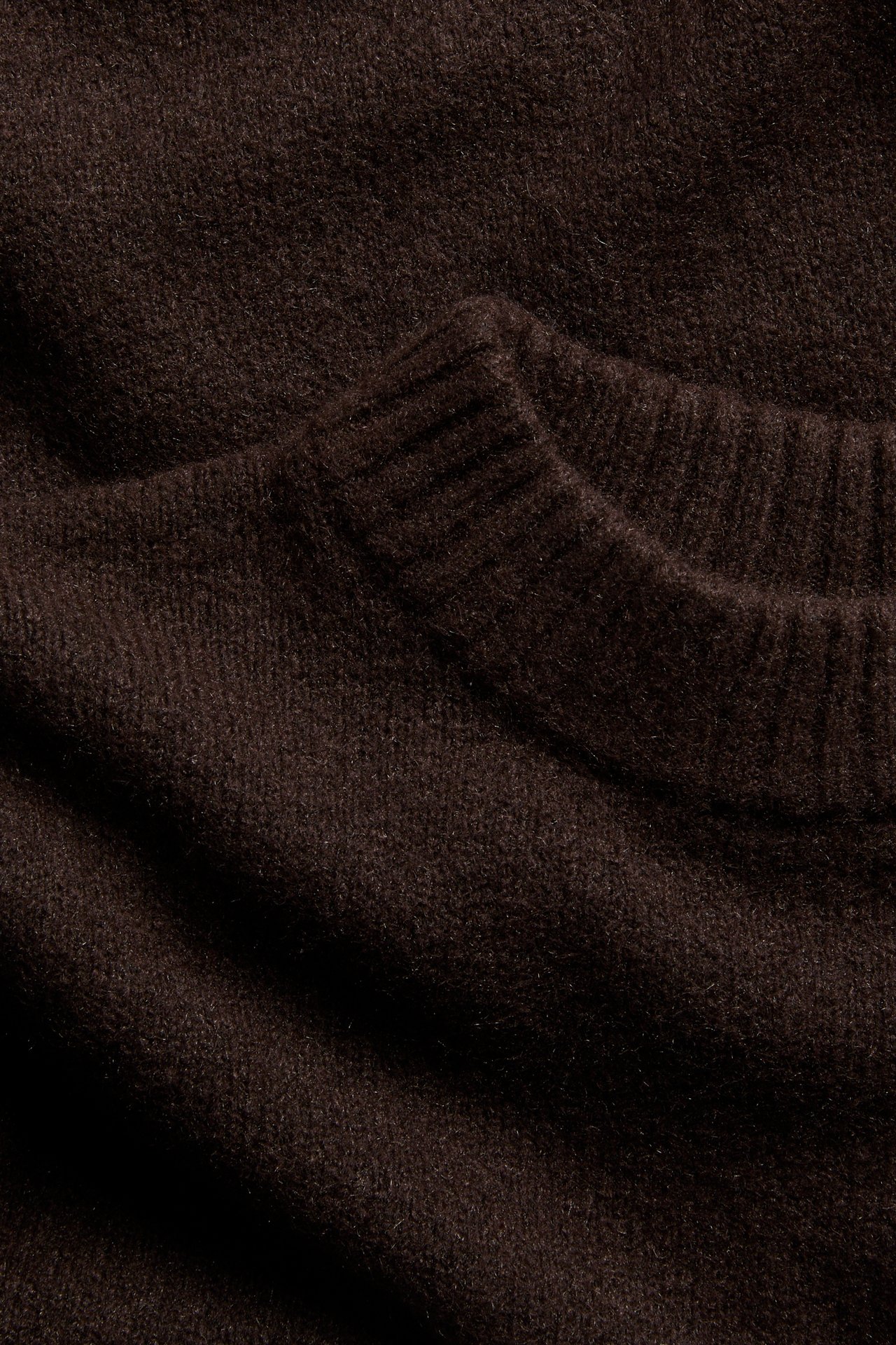 Närbild av en mörkbrun melerad stickad rundhalsad pullover.