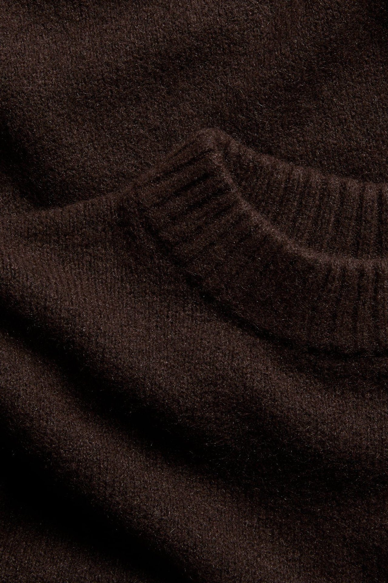 Närbild av en mörkbrun melerad stickad rundhalsad pullover.