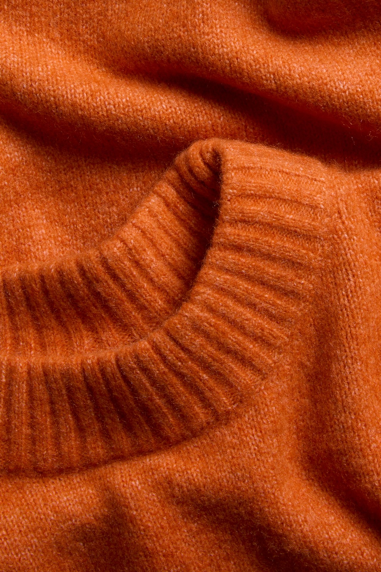 Närbild av en orange melerad stickad rundhalsad tröja.