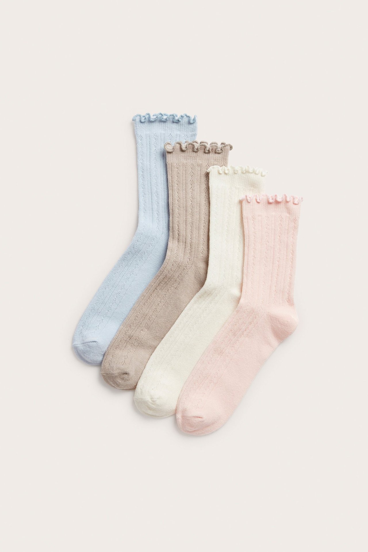Vinklad frontvy av fyra par pointellestickade strumpor i ljusrosa, benvit, ljusbrun och ljusblå med volangkant.