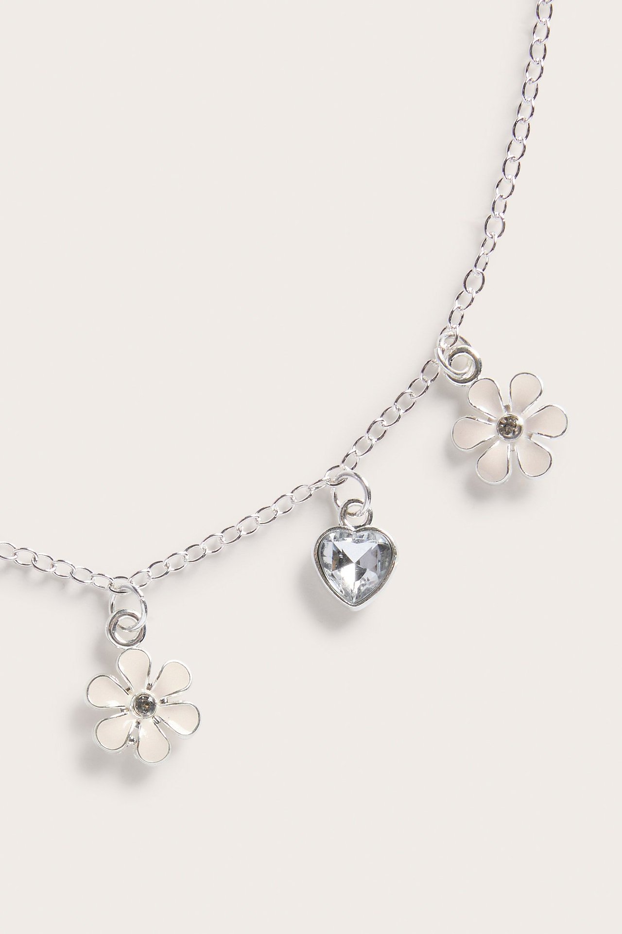 Lähikuva hopeaketjusta, jossa kaksi valkoista emalikukkariipusta ja yksi kirkas sydänriipus.