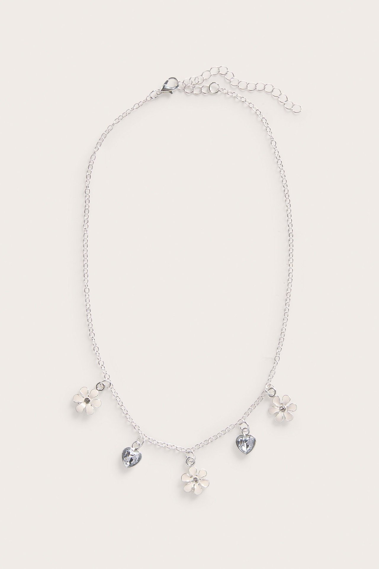 Hopeanvärinen kaulakoru valkoisilla kukkakoruilla ja kirkkailla sydänriipuksilla, ylhäältä kuvattu.