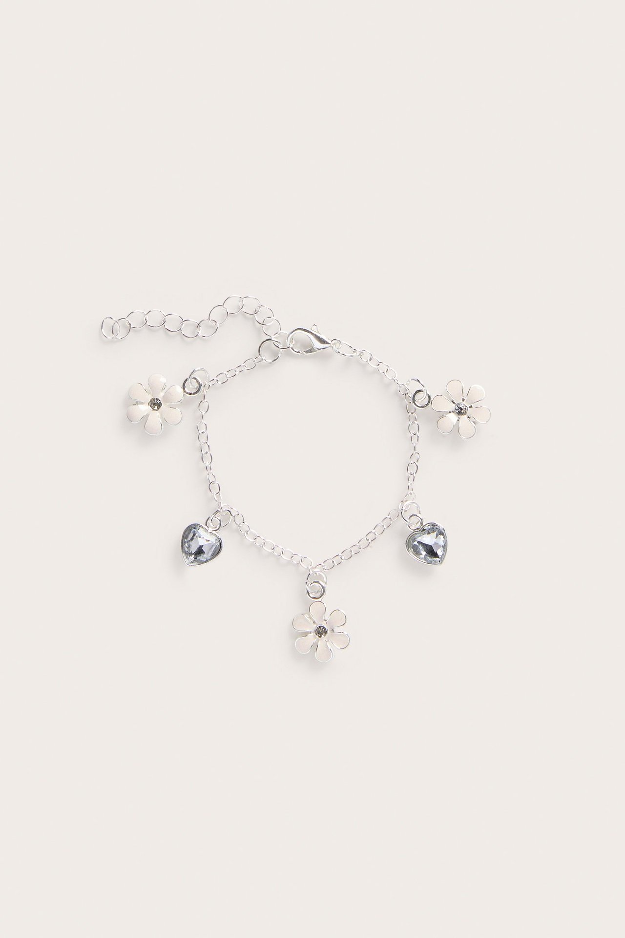 Ylhäältä kuvattu hopeanvärinen metallirannekoru, jossa valkoisia kukkia ja vaaleansinisiä sydänkoruja.