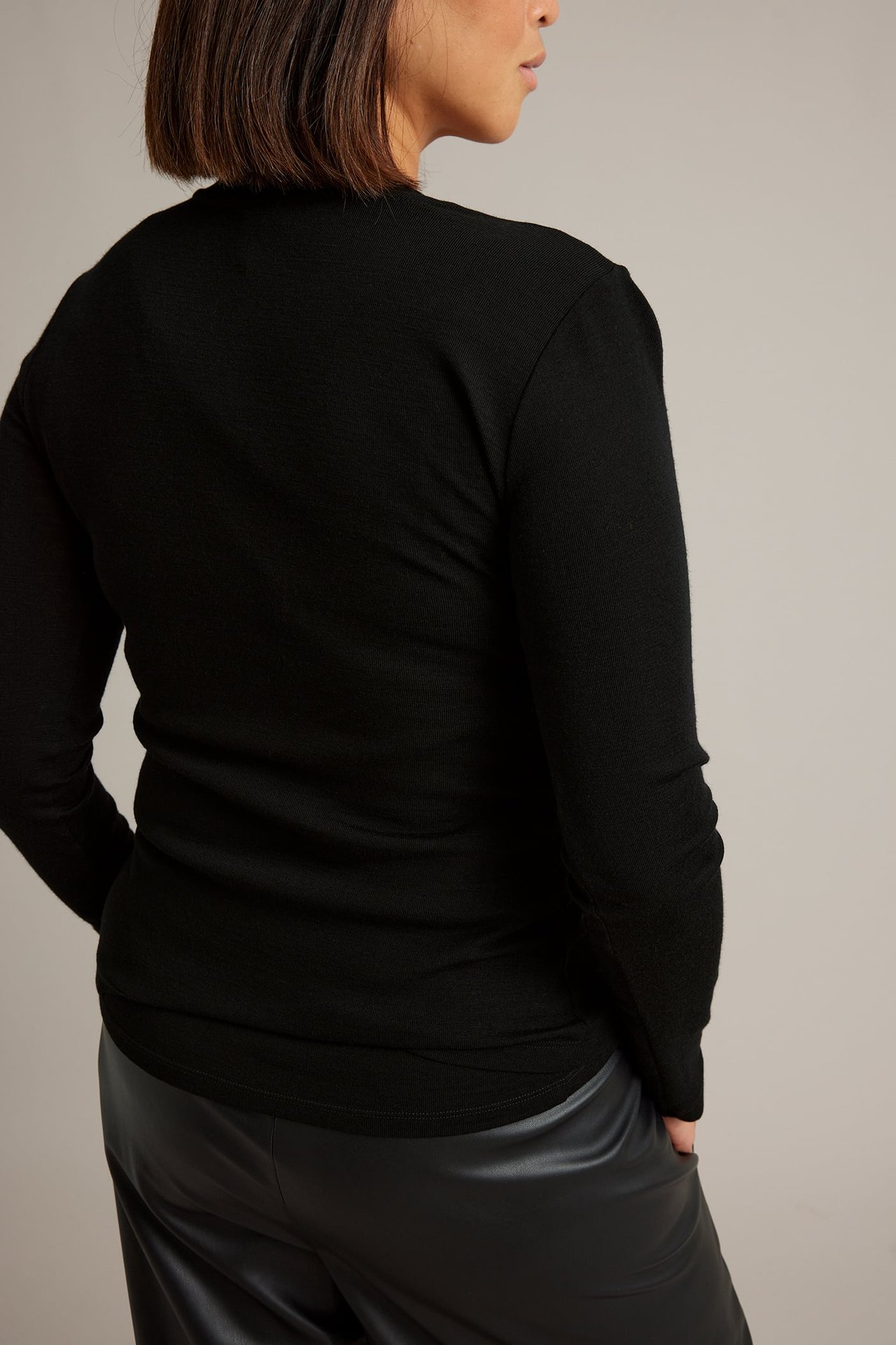 Kvinnlig modell, bakifrån, i svart texturerad långärmad topp och svarta läderbyxor.