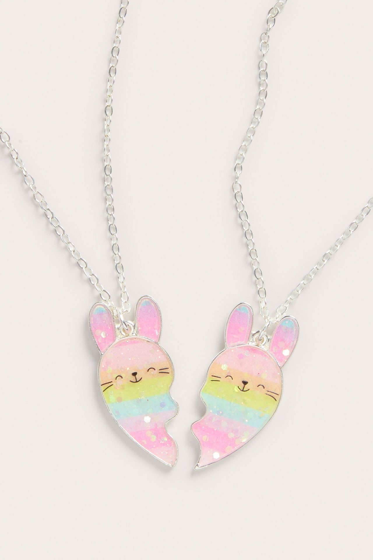 Zbliżenie na dwa srebrne naszyjniki przyjaźni z brokatowymi tęczowymi zawieszkami w kształcie króliczych serc.