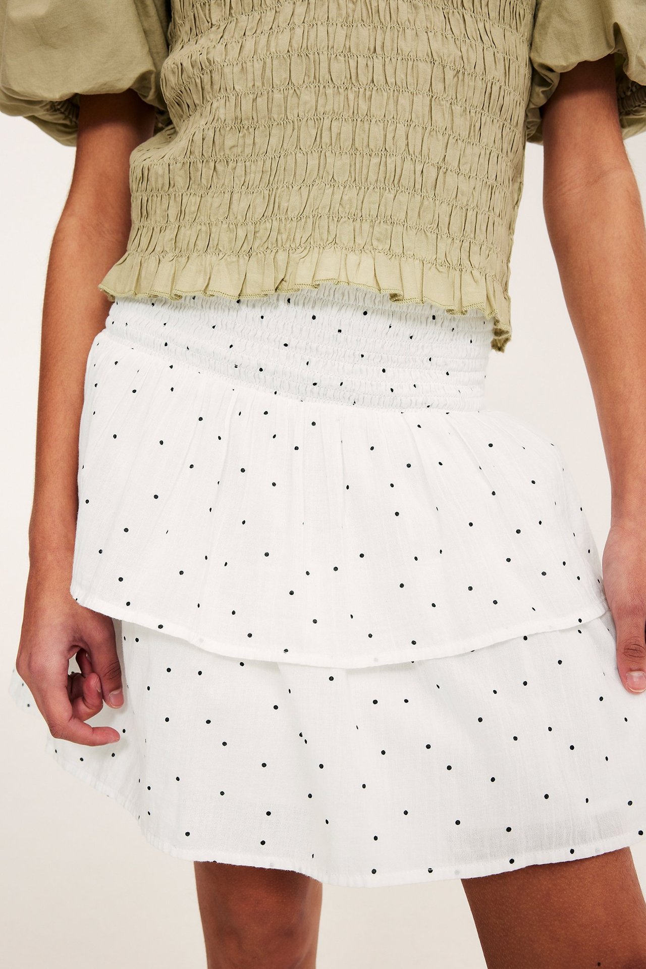 Front view: Kid in vit prickig volangkjol med smockmidja och en grön smockad crop top.