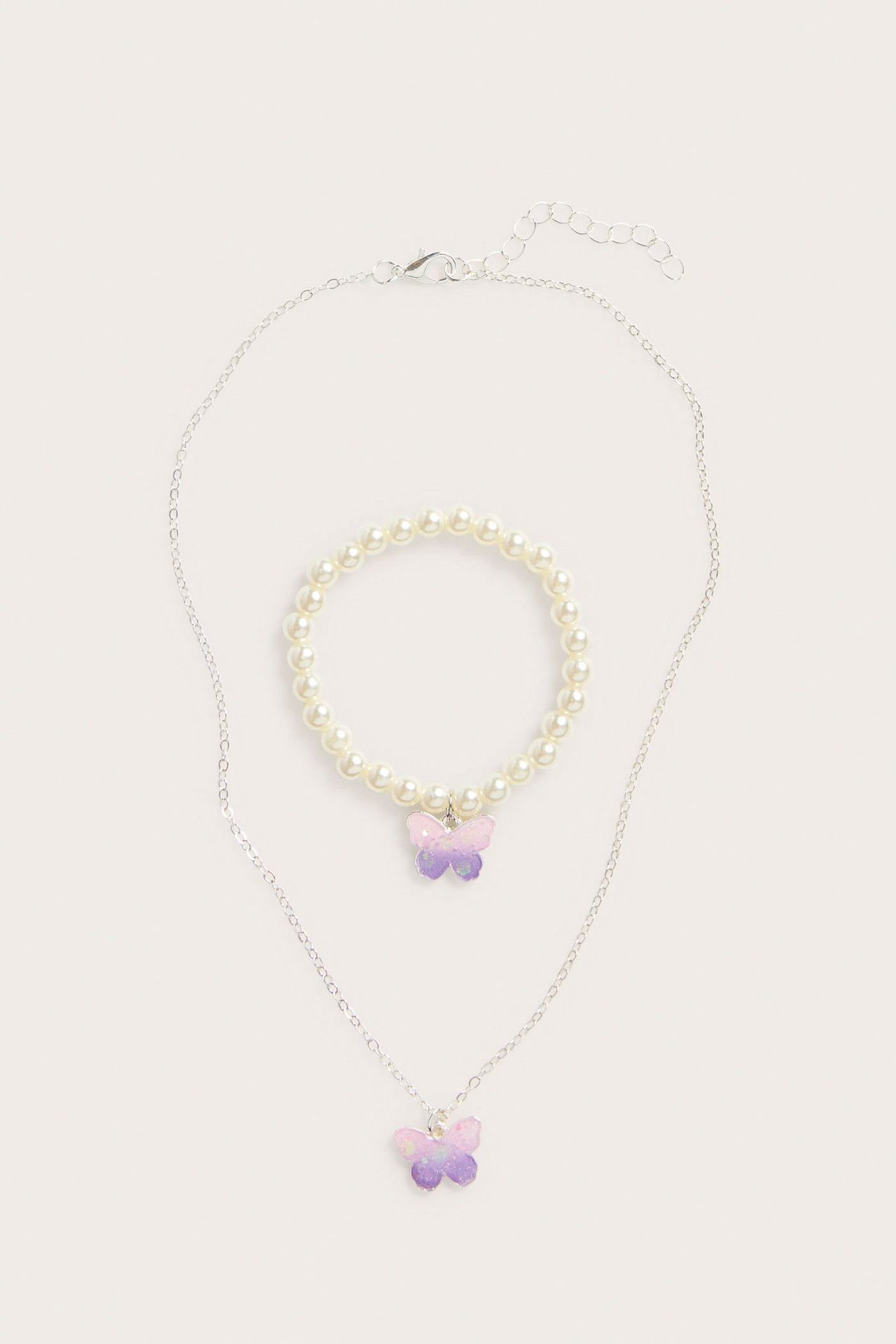 Barnesmykkesett: sølvkjede med lilla-rosa sommerfuglanheng og hvitt perlearmbånd.