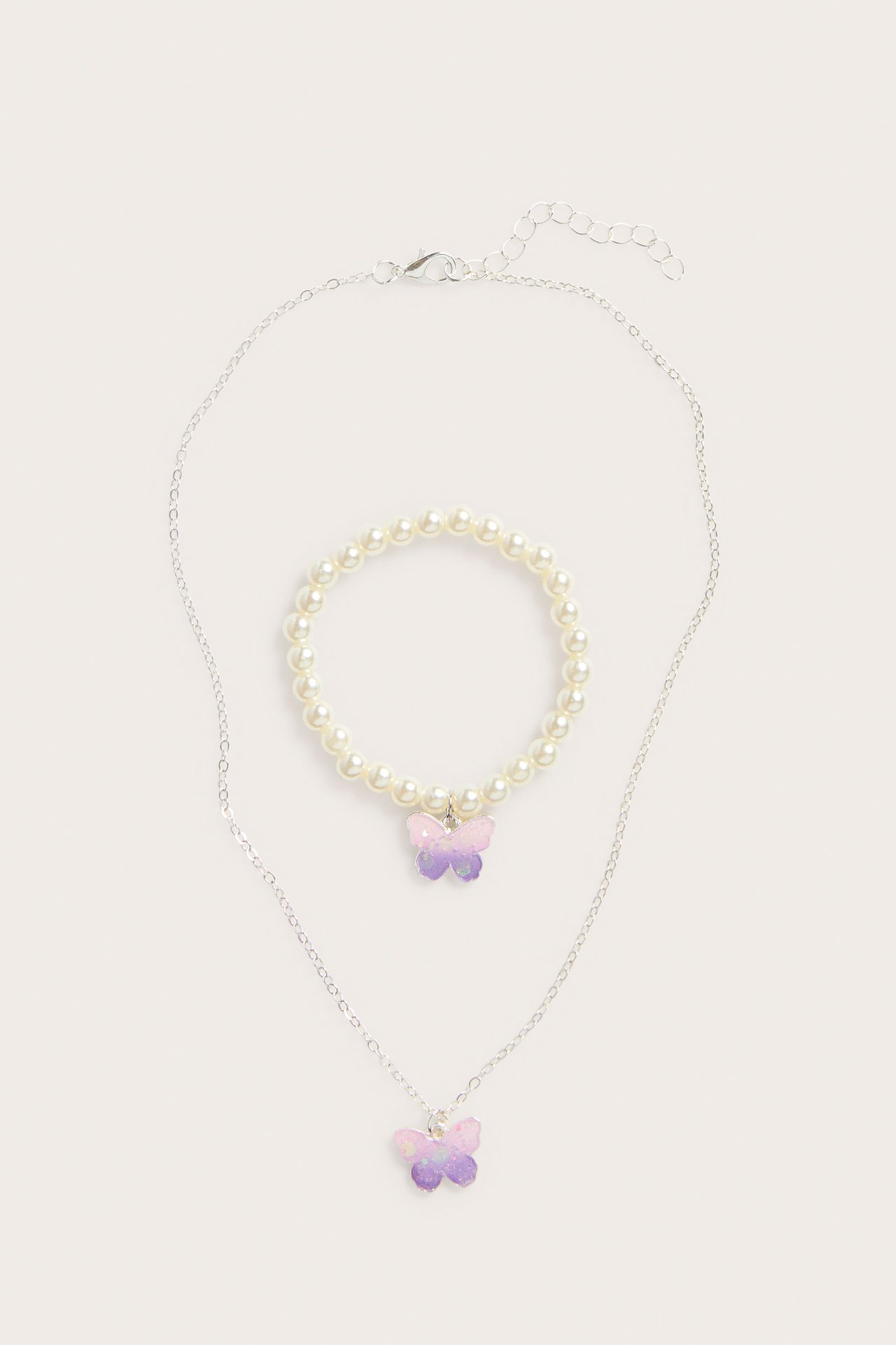 Zestaw biżuterii dla dzieci: srebrny naszyjnik z fioletowo-różowym motylem i biała perłowa bransoletka.