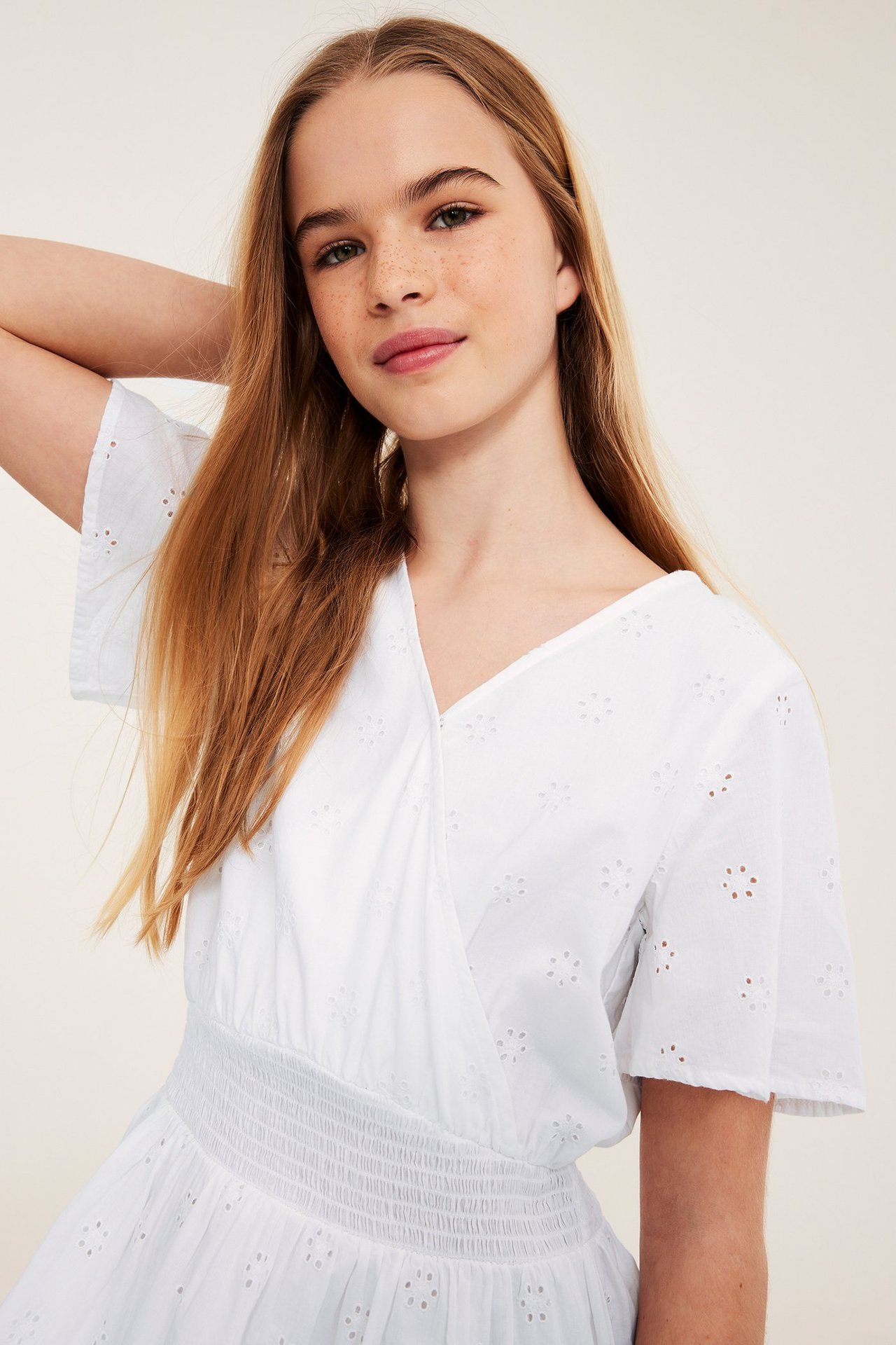 Edestä, lapsi valkoisessa puuvillamekossa, jossa reikäkuvio, kietaisuyläosa ja smokkivyötärö.