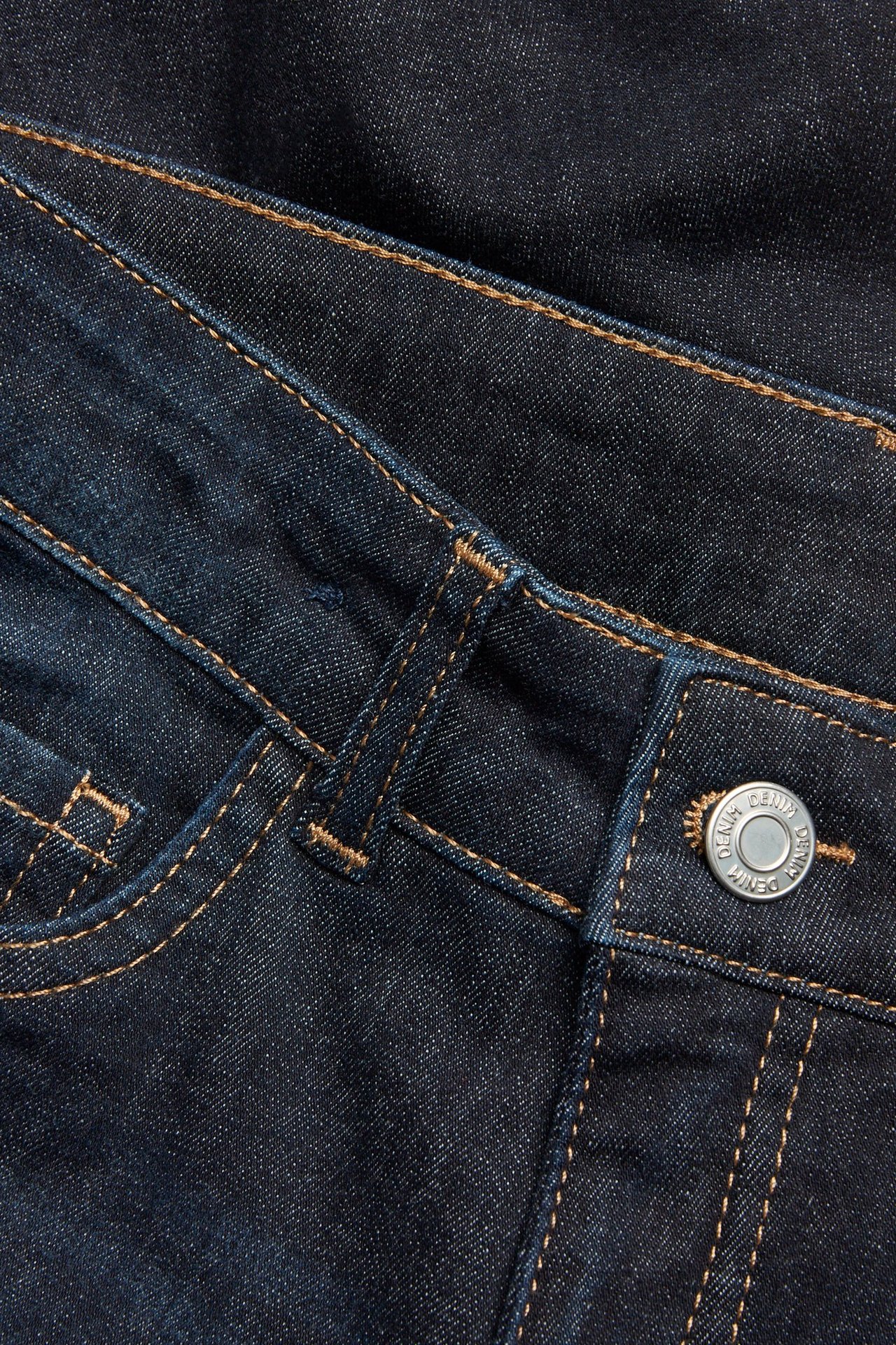 Zbliżenie na ciemnoniebieskie jeansy bootcut z pomarańczowymi szwami i srebrnym metalowym guzikiem.