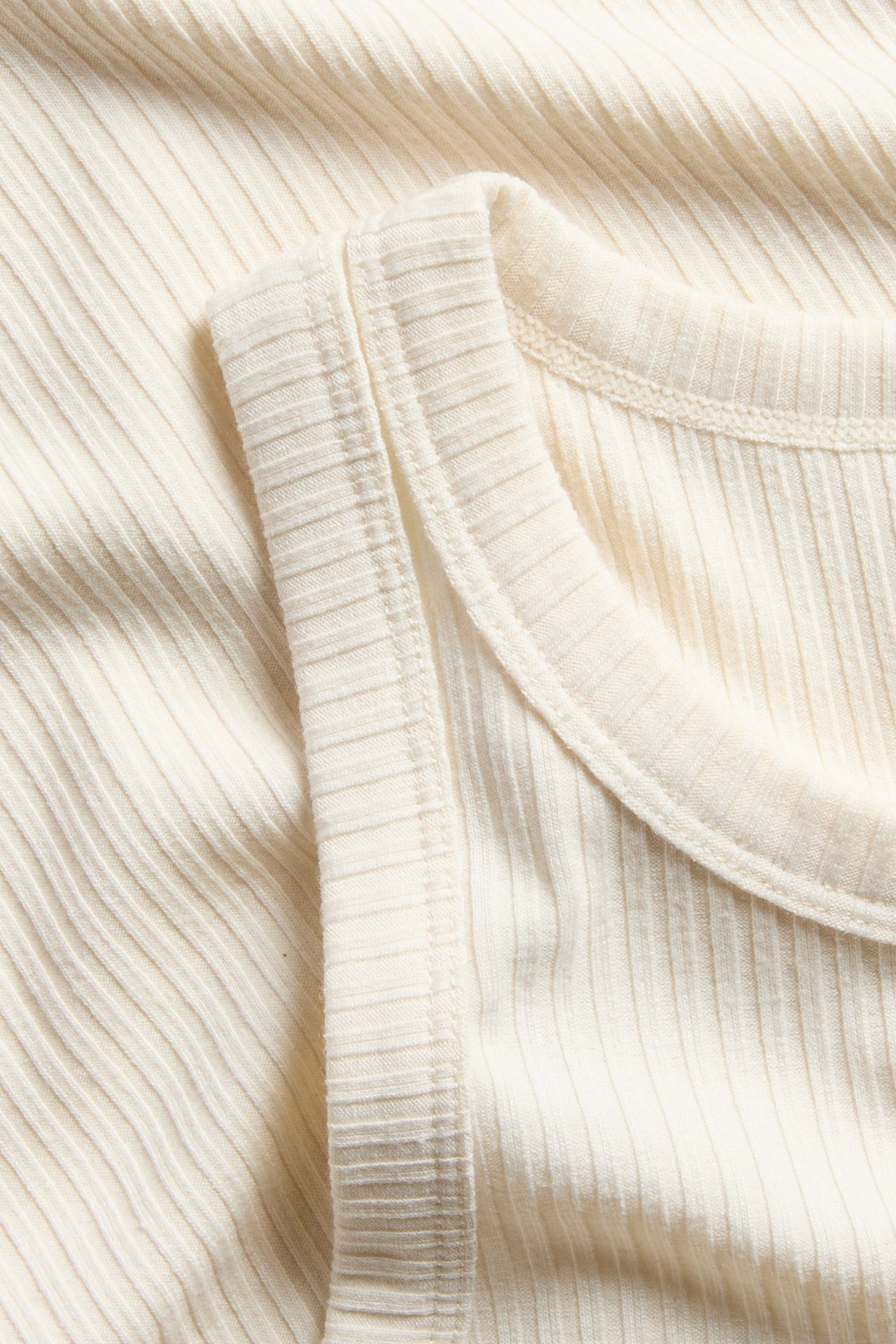 Närbild av ett offwhite ribbat linne, som visar det strukturerade tyget och halsringningsdetaljer.
