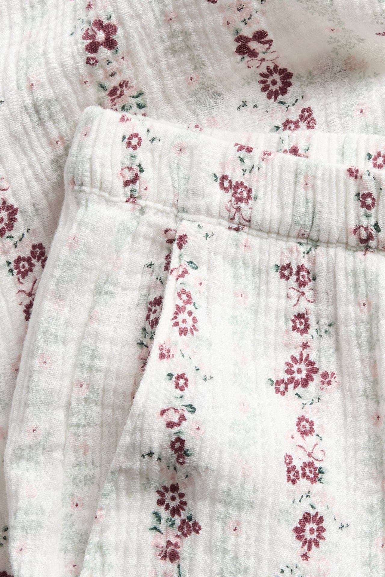 Närbild på vit krinklad pyjamas med vinrött och rosa blommönster och resår i midjan.